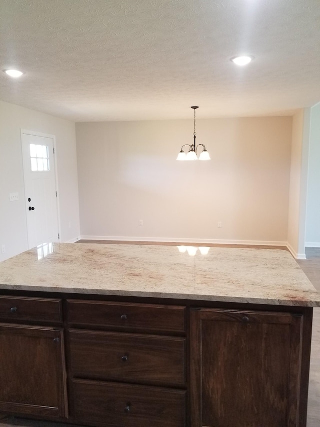 kitchen featuring light stone countertops, dark brown cabinets, a textured ceiling, pendant lighting, and a chandelier