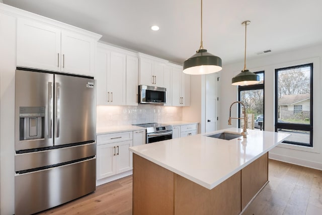 kitchen with stainless steel appliances, sink, a center island with sink, white cabinets, and hanging light fixtures