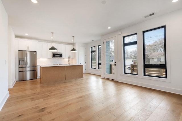 kitchen with white cabinets, appliances with stainless steel finishes, a center island with sink, and a healthy amount of sunlight