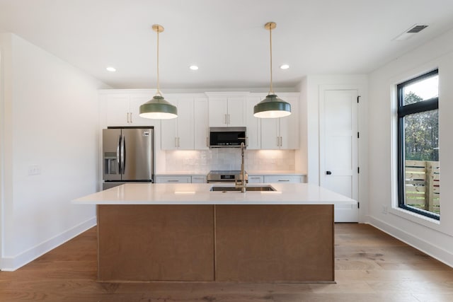 kitchen featuring white cabinets, plenty of natural light, a center island with sink, and stainless steel appliances