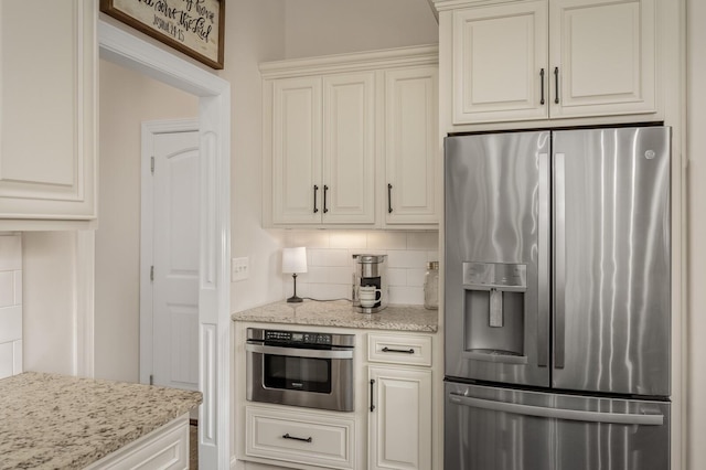 kitchen with stainless steel appliances, light stone counters, tasteful backsplash, and white cabinetry