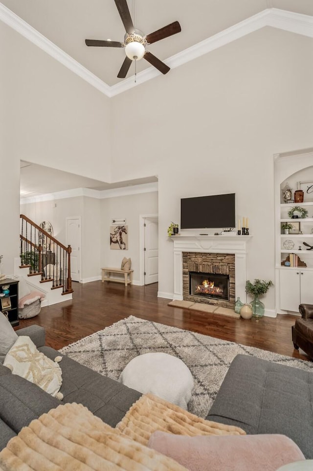 living room with ceiling fan, a stone fireplace, dark hardwood / wood-style flooring, high vaulted ceiling, and ornamental molding