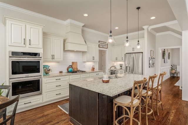 kitchen featuring a center island with sink, sink, dark hardwood / wood-style floors, light stone countertops, and appliances with stainless steel finishes