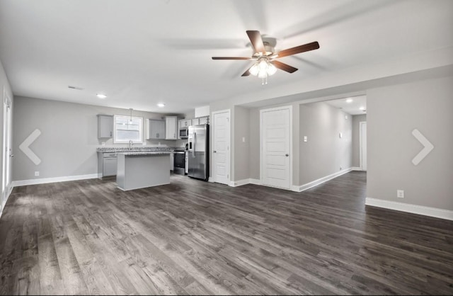 unfurnished living room with dark wood-style floors, a ceiling fan, and baseboards