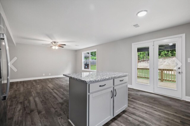 kitchen with visible vents, light stone counters, a center island, ceiling fan, and dark wood-style flooring