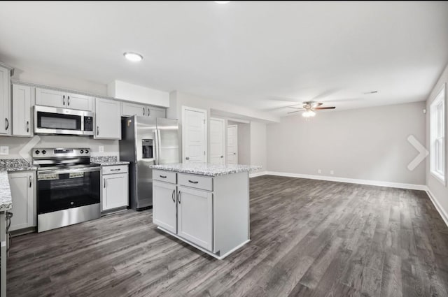 kitchen featuring dark wood finished floors, a center island, appliances with stainless steel finishes, baseboards, and ceiling fan