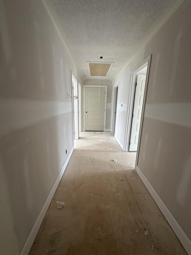 corridor featuring attic access, baseboards, and a textured ceiling