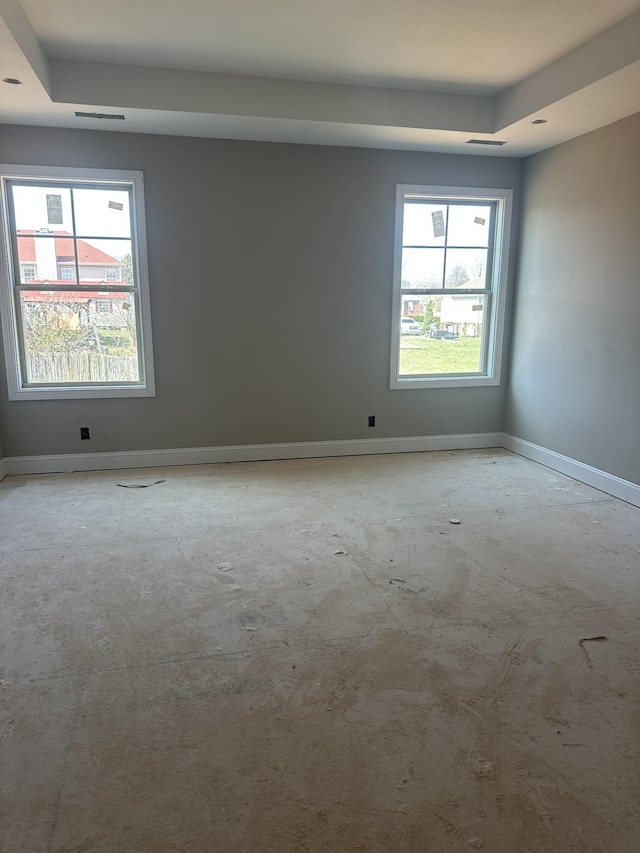 spare room featuring a tray ceiling, a healthy amount of sunlight, and baseboards