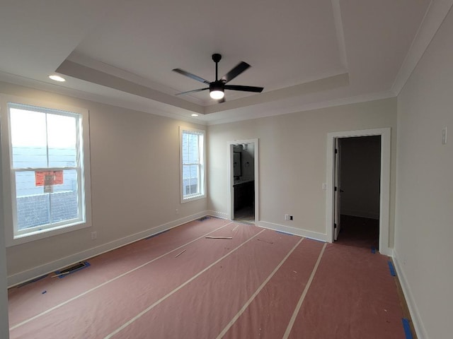 unfurnished bedroom featuring a tray ceiling, a walk in closet, crown molding, and multiple windows