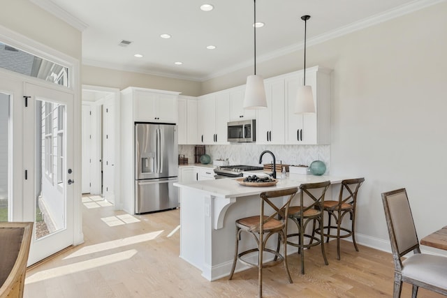 kitchen featuring kitchen peninsula, a breakfast bar, stainless steel appliances, white cabinetry, and hanging light fixtures