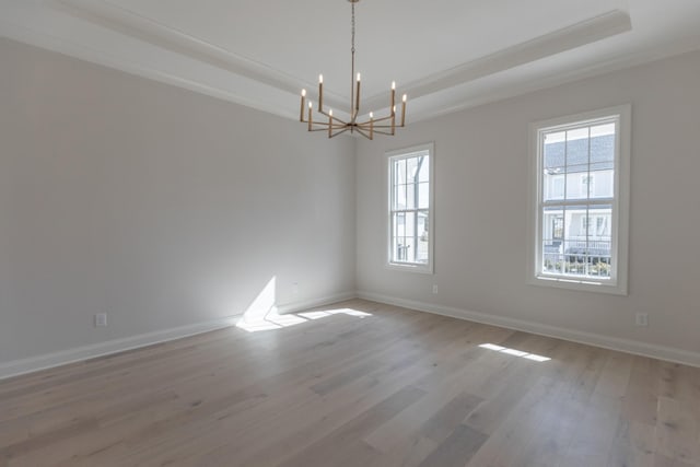 unfurnished room with baseboards, a tray ceiling, light wood-style floors, crown molding, and a notable chandelier