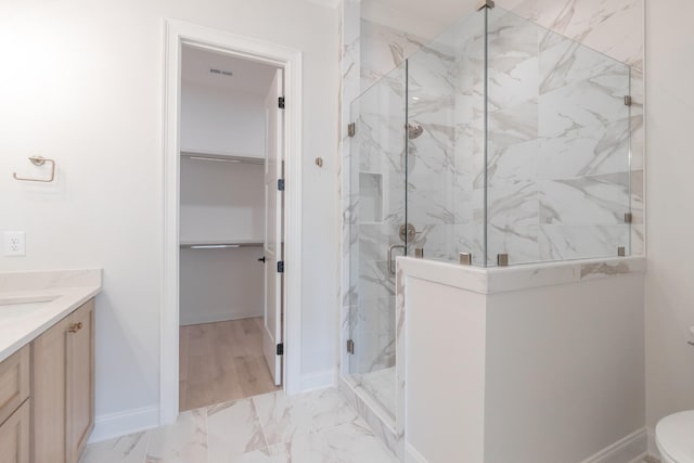 bathroom featuring marble finish floor, a marble finish shower, vanity, baseboards, and a spacious closet