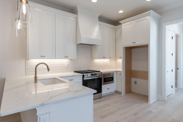 kitchen featuring premium range hood, a sink, white cabinetry, stainless steel range with gas cooktop, and a peninsula