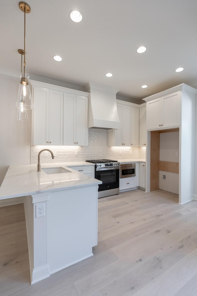 kitchen featuring backsplash, stainless steel range with gas cooktop, premium range hood, a peninsula, and a sink