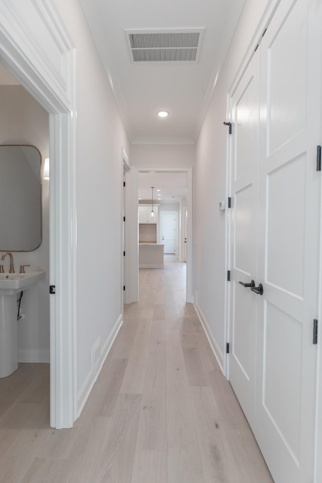 corridor with visible vents, baseboards, light wood-style flooring, and ornamental molding