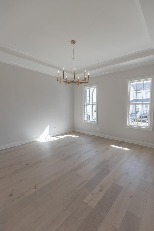 empty room with a tray ceiling, baseboards, light wood-style floors, and an inviting chandelier