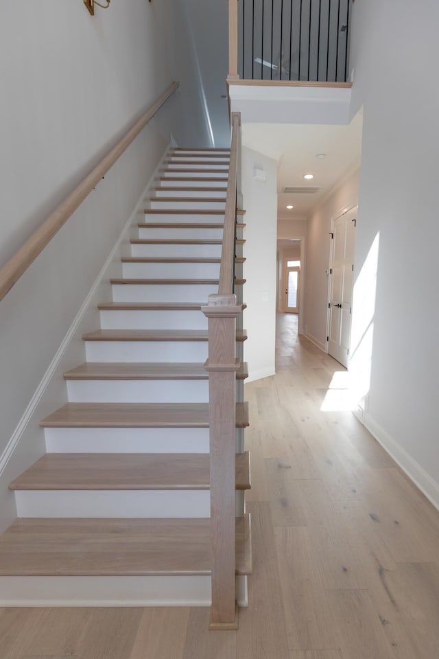 staircase featuring recessed lighting, wood finished floors, baseboards, and a towering ceiling