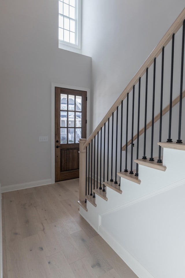 entryway with light wood-type flooring, stairway, baseboards, and a high ceiling