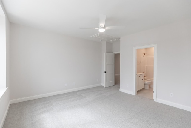 unfurnished bedroom with baseboards, ceiling fan, light colored carpet, attic access, and ensuite bathroom