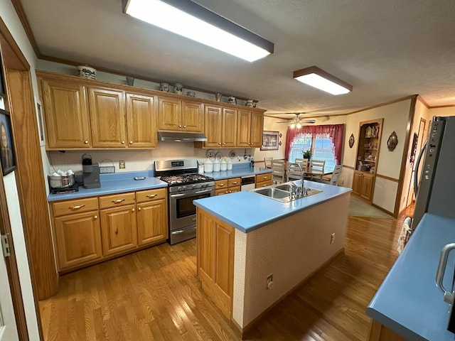 kitchen with ceiling fan, sink, stainless steel range with gas cooktop, light hardwood / wood-style floors, and a center island with sink