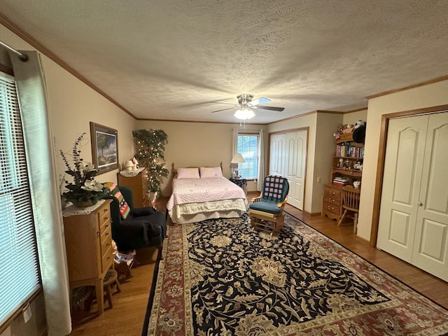 bedroom featuring a textured ceiling, ceiling fan, crown molding, wood-type flooring, and multiple closets