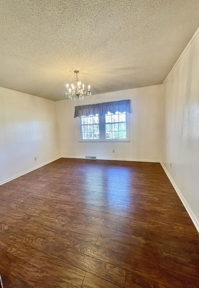 spare room featuring a chandelier, dark wood-type flooring, and a textured ceiling