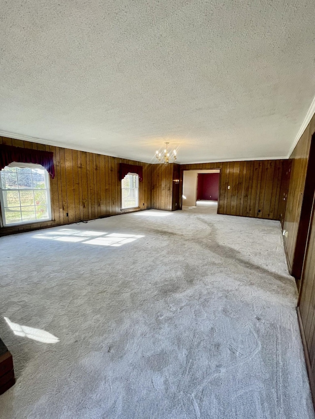 carpeted empty room featuring a chandelier, a textured ceiling, and wood walls