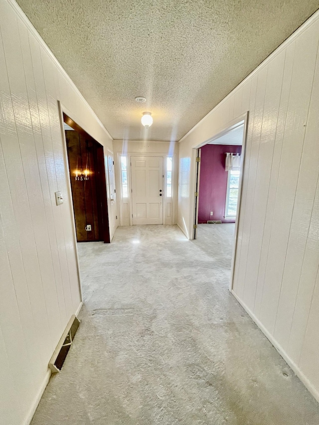 hallway with light carpet, a textured ceiling, and wood walls