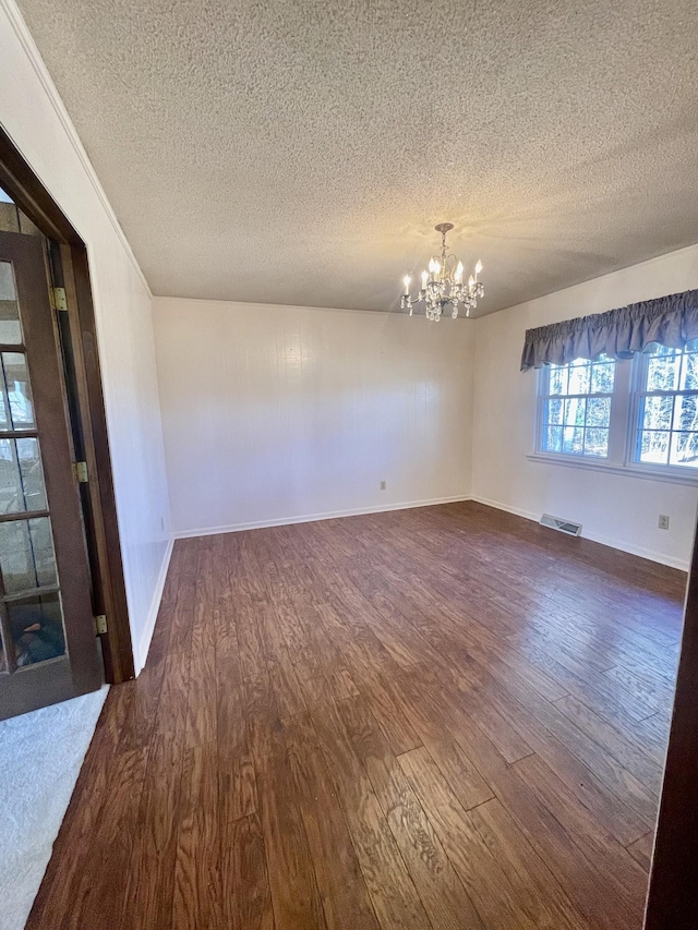 spare room featuring a notable chandelier, dark hardwood / wood-style flooring, and a textured ceiling