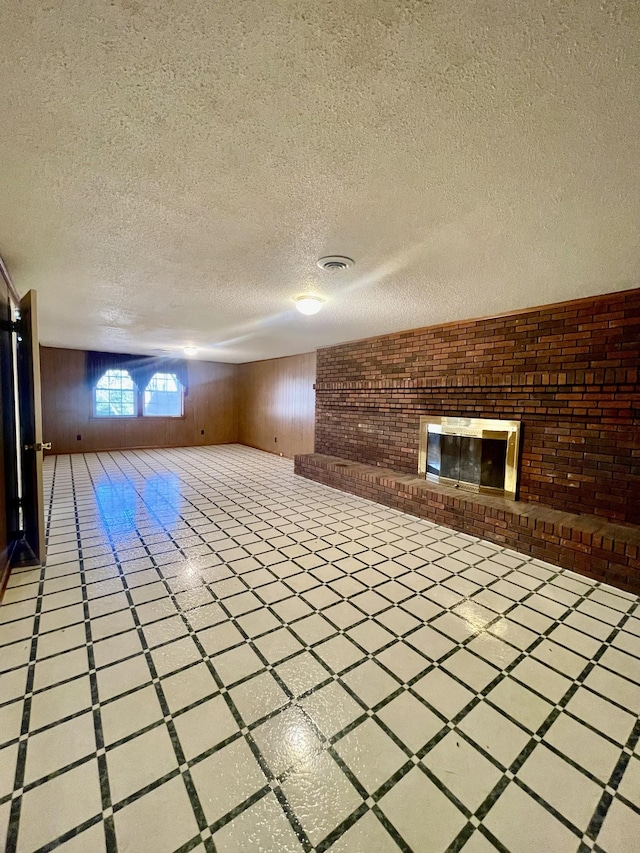 basement featuring a textured ceiling, wooden walls, and a brick fireplace