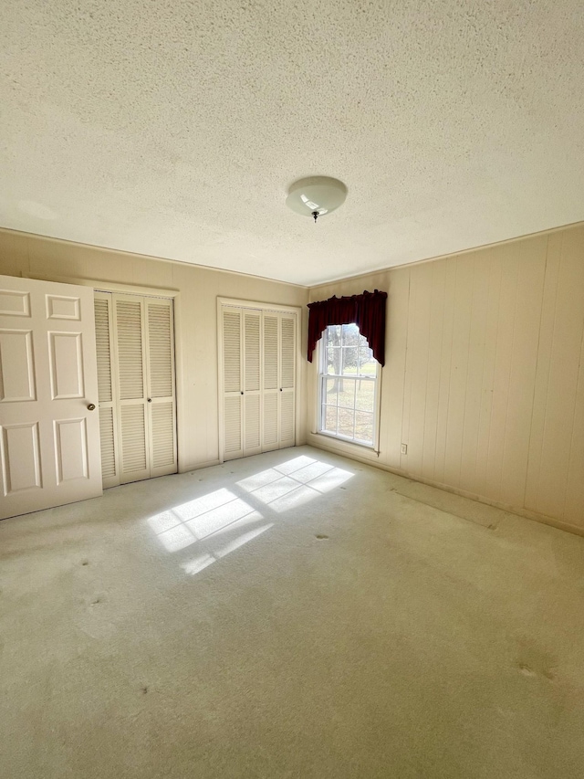 unfurnished bedroom featuring carpet flooring, a textured ceiling, two closets, and wooden walls