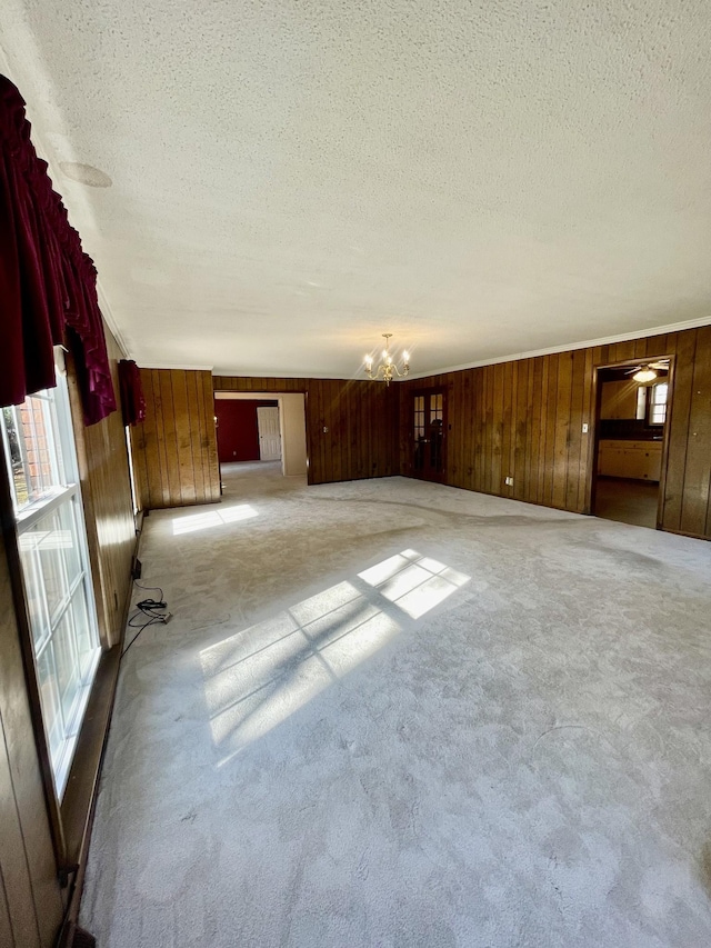 unfurnished living room featuring plenty of natural light, light colored carpet, wooden walls, and an inviting chandelier