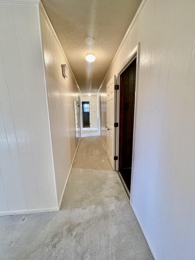 hallway featuring light carpet, a textured ceiling, ornamental molding, and wood walls