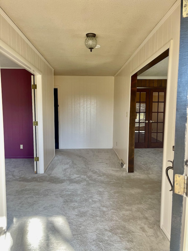 hallway with wood walls, french doors, crown molding, a textured ceiling, and light colored carpet