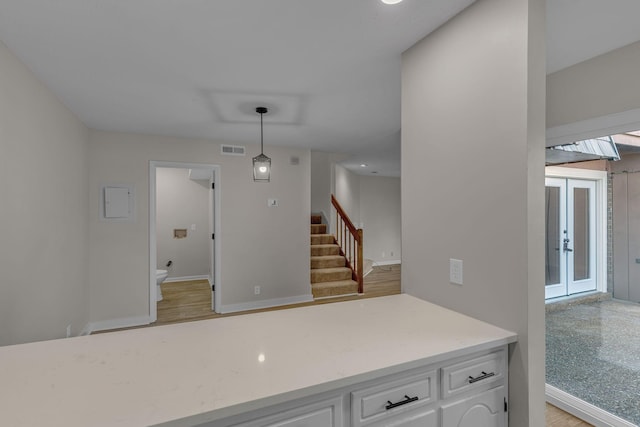 kitchen with white cabinetry, french doors, hanging light fixtures, and light wood-type flooring