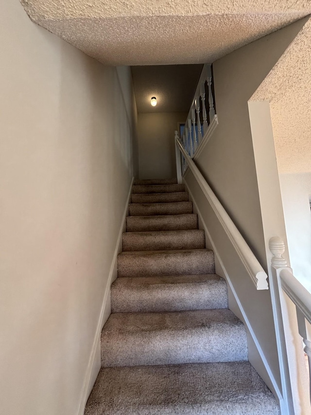 stairway featuring a textured ceiling and carpet floors