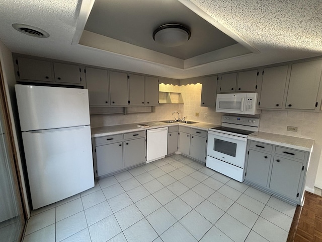 kitchen featuring gray cabinets, a raised ceiling, white appliances, and sink