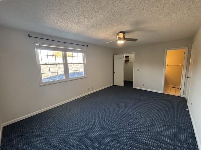 unfurnished bedroom featuring a spacious closet, a closet, ceiling fan, and dark colored carpet