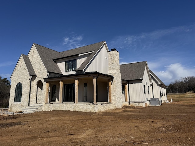 view of side of home featuring central air condition unit, covered porch, roof with shingles, board and batten siding, and a chimney