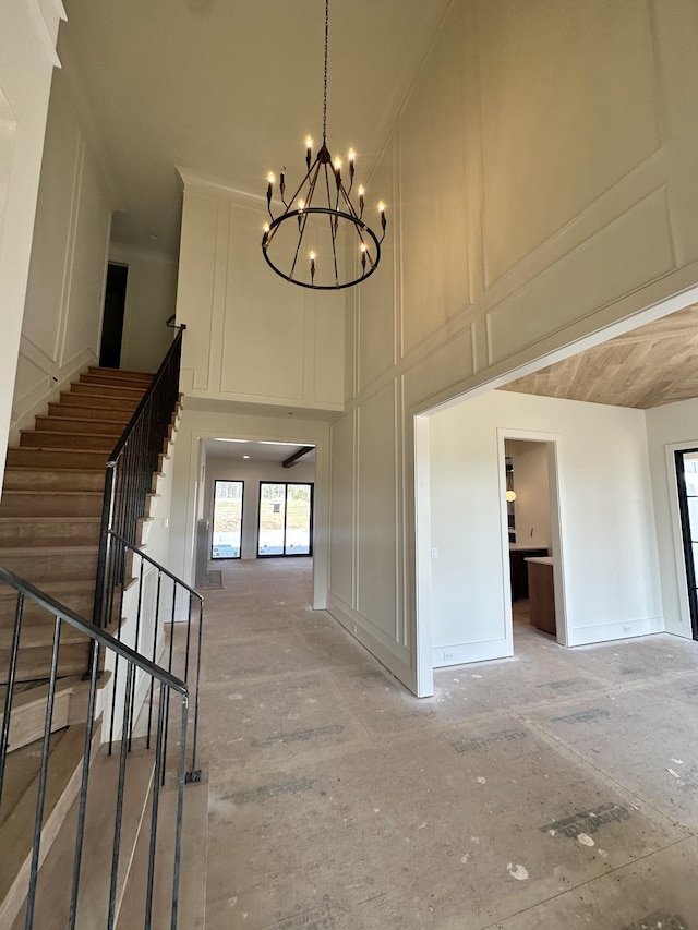 corridor with a notable chandelier, a decorative wall, a towering ceiling, and stairs