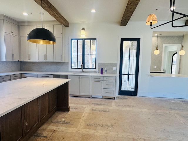 kitchen featuring hanging light fixtures, backsplash, a sink, light stone countertops, and beamed ceiling