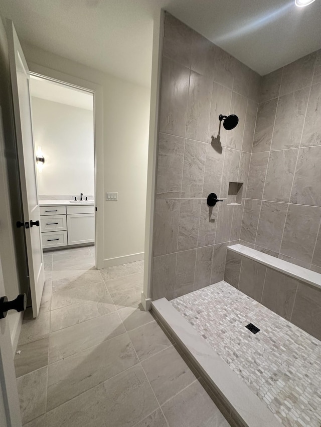 full bathroom with tiled shower, vanity, and baseboards