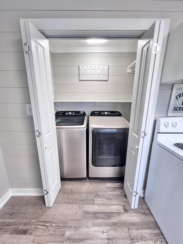 laundry room with light hardwood / wood-style floors, washer and clothes dryer, and wood walls