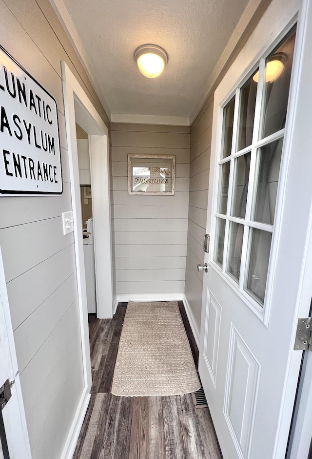 doorway to outside featuring a textured ceiling, wood walls, and dark wood-type flooring