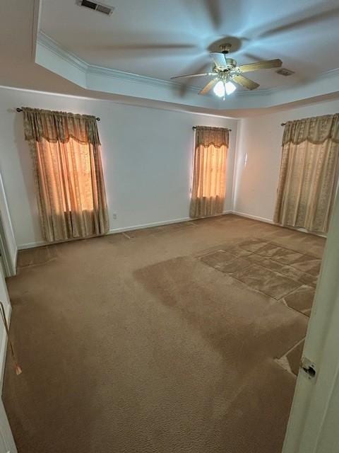 carpeted spare room with a raised ceiling, ceiling fan, plenty of natural light, and ornamental molding