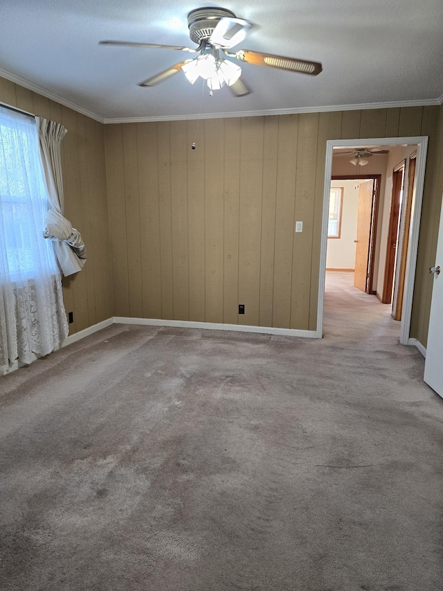 spare room with ceiling fan, wood walls, light colored carpet, and ornamental molding