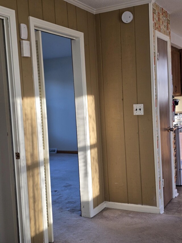 hall with wooden walls, light colored carpet, and crown molding