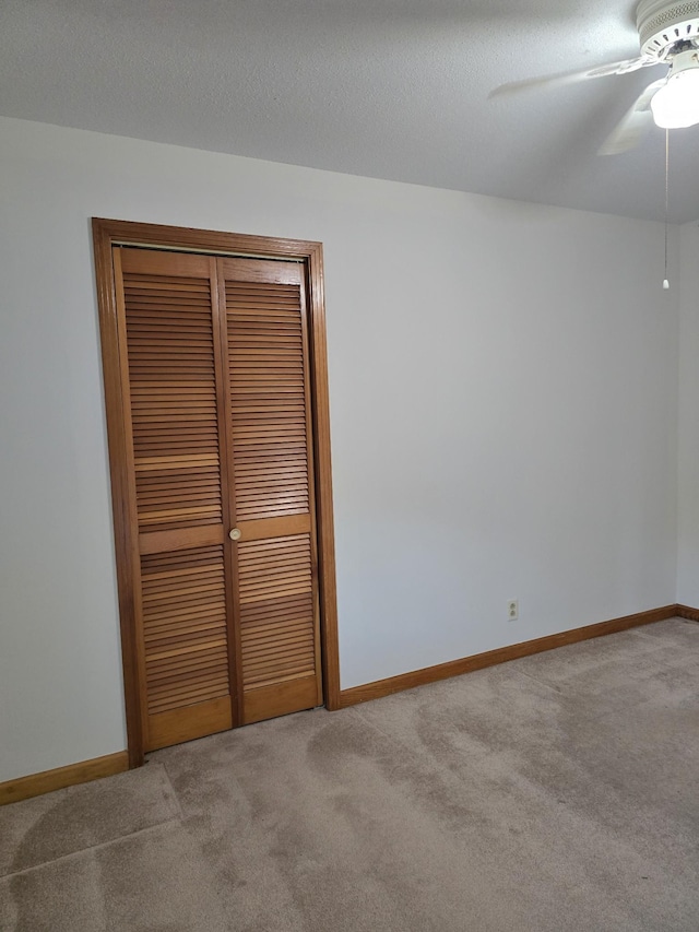 unfurnished bedroom with ceiling fan, a closet, light colored carpet, and a textured ceiling