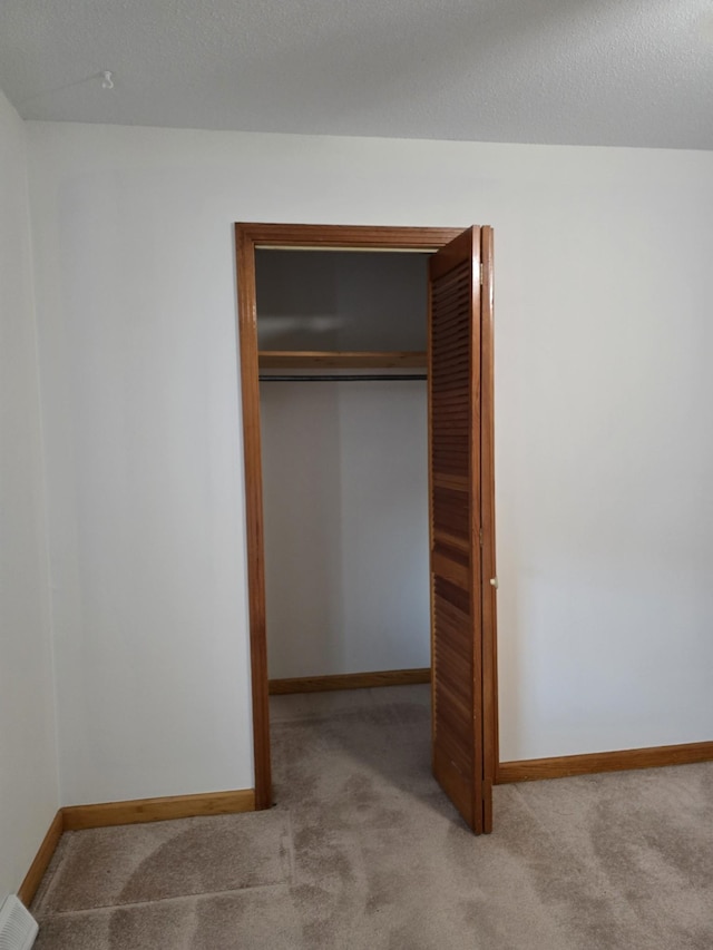 unfurnished bedroom with a closet, light colored carpet, and a textured ceiling