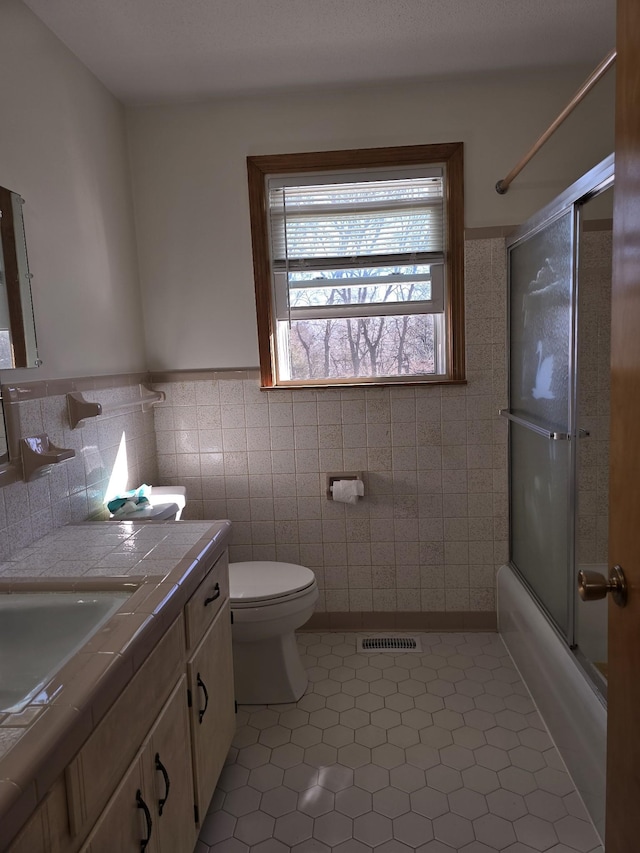 full bathroom featuring tile patterned floors, vanity, tile walls, enclosed tub / shower combo, and toilet